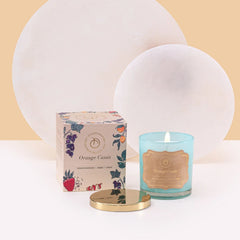 Illume Midi - Lid Jar Candle - Aqua - Orange Cassis - Set of 2, lit aqua glass jar with gold lid beside Orange Cassis box