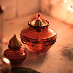 Two amber-colored glass Kalash Oil Lamps with a diya on a reflective surface.