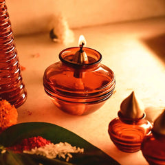 Amber glass oil lamp with a flame on a light-colored surface, surrounded by decorative elements.