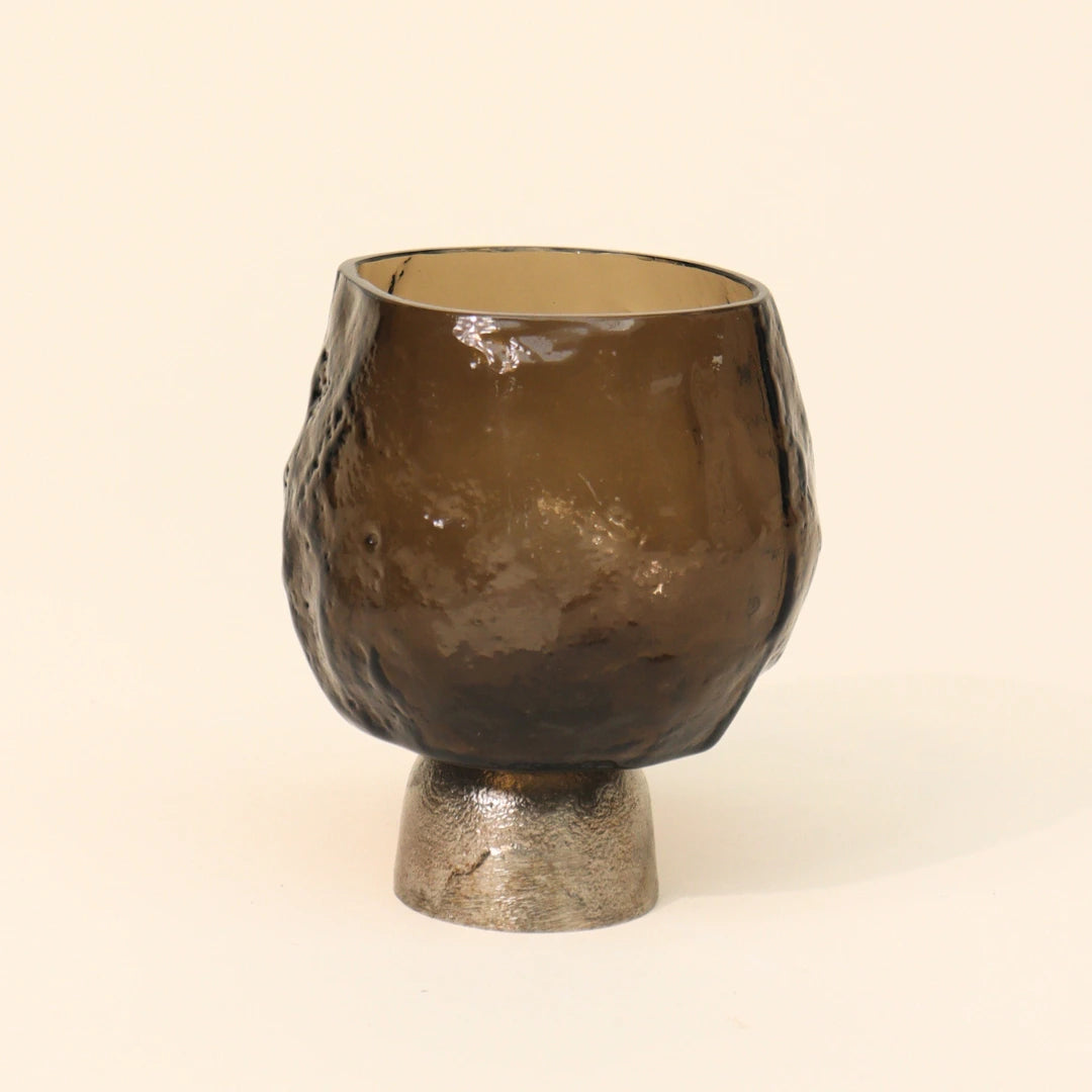 Brown glass candle holder with sandcast metal base on a beige background