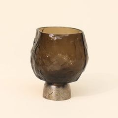 Brown glass candle holder with sandcast metal base on a beige background