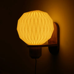 Aura Pleat Linen Wall Sconce. Close-up of origami pleated linen shade glowing light