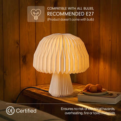 A pleated mushroom-shaped Origami table lamp glowing warm white on a wooden table, with text overlays stating compatibility with E27 bulbs and a CE Certified mark.