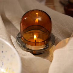 Muun Dome Tealight Holder in amber, lit tealight glowing through borosilicate glass dome, close-up on linen
