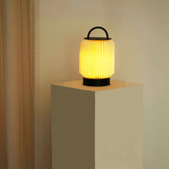 Tote Table Lamp, portable with black handle on a beige pedestal against a beige wall