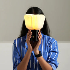 Person holding a portable paper bouquet Table Lamp with a yellow light against a neutral background