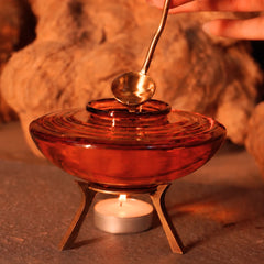 Muun Ghee Daani with lit tealight beneath amber glass pot, spoon lifted from brass lid, close-up