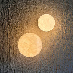 Two spherical moon-style wall sconces with a textured, alabaster stone emit a warm golden glow against a textured wall.