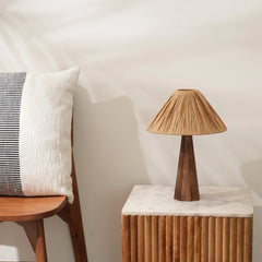 A Harmony Table Lamp with a wooden base and a beige, empire-shaped raffia shade, placed on a wooden side table.