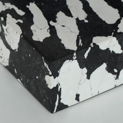 A close-up of a black and white  box corner, showing a textured stone-like pattern on a light gray background.