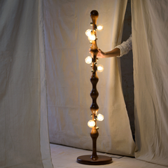 A tall, sculptural stem floor lamp with a dark brown twisted wood-like base and multiple glowing warm white globe bulbs.