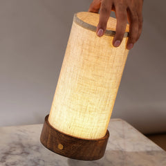 Unique cylindrical portable magnus table lamp with a beige shade and a wooden base.