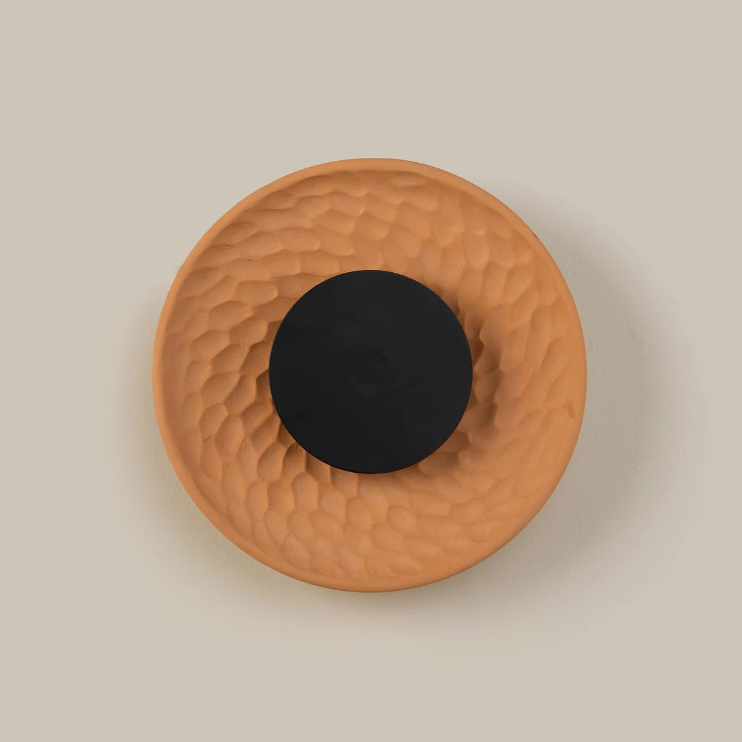 Round terracotta Disc Wall Light with a black center on a beige background