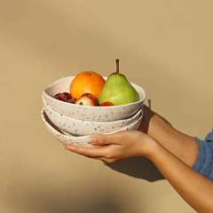 A person holding round Speckled Ceramic bowls with a speckled pattern, featuring a blend of white base, red & blue speckles.
