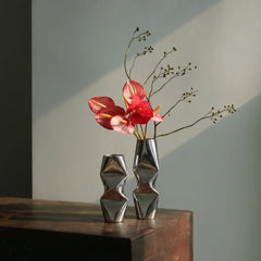 Two metallic silver geometric flower vases on a dark wooden table, holding red flowers.