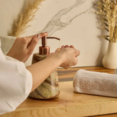 Reen Soap Dispenser, a marble-patterned with a metallic copper pump on a wooden table, with a white towel and dried grass in the background.