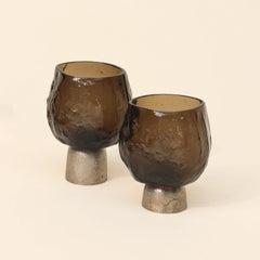 Two brown glass candle holders with metallic bases on a beige background