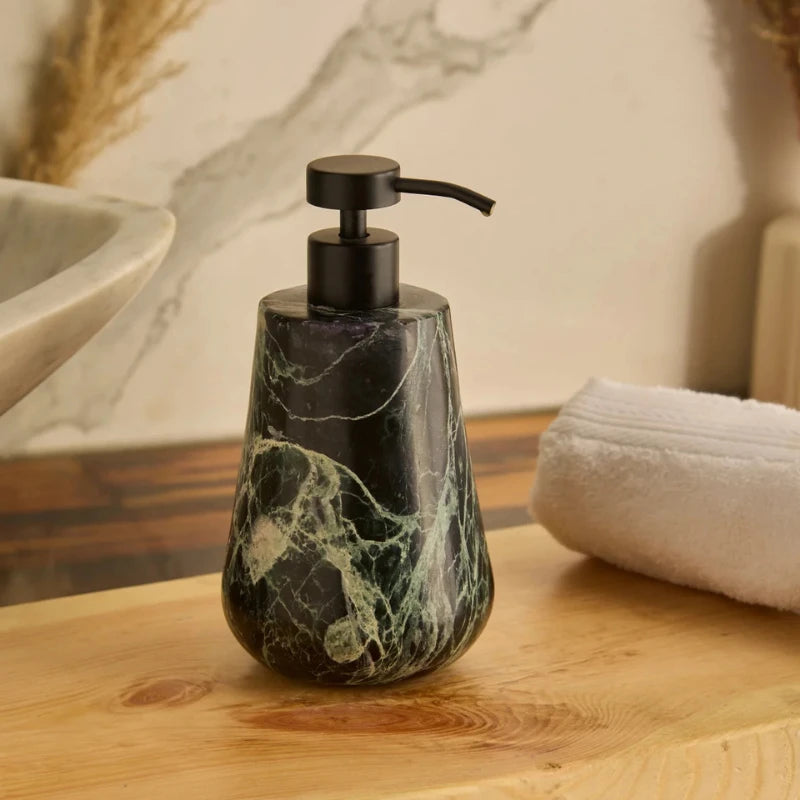 A teardrop-shaped Spyder soap dispenser with a black metal pump and a dark green and black marble body, sitting on a wooden bathroom counter next to a white towel.