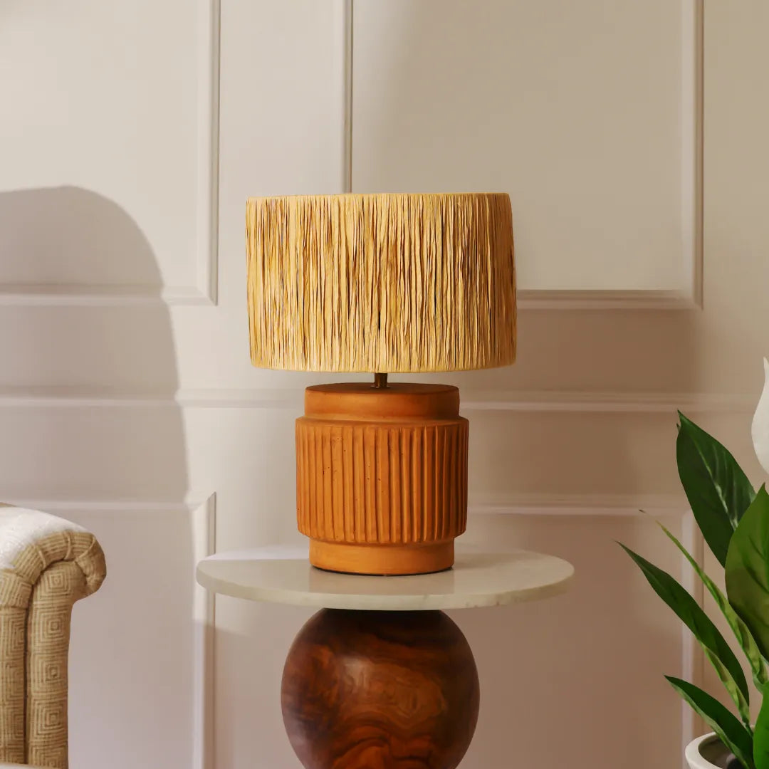 Wooden Dune Table Lamp with a textured raffia shade & terracotta base on a small round table against a neutral wall.