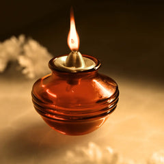 Traditional oil lamp with a burning wick on a reflective surface.