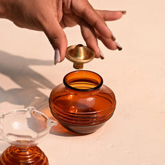 Hand holding an amber-colored glass container with a gold oil lamp on a beige background
