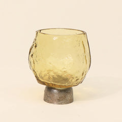 Yellow glass candle holder with Sandcast metal base on a beige background