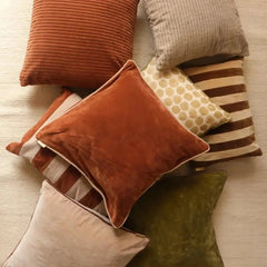 A styled arrangement of multiple decorative velvet cushion covers in warm neutral and earthy tones