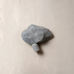 A gray stone wall hook shaped like a small rock with a cylindrical peg, mounted on a textured beige plaster wall.