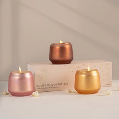 Three lit mini scented Votive Candle set in metallic rose gold, gold, and copper finish in Opulent Oud fragrance are arranged in front of their cream-colored gift box.