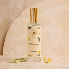 Illume - Room Freshener - 100 ML, Wild Lemongrass spray bottle with gold cap beside lemongrass stalks