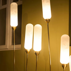 Close look of Kinara outdoor floor lamp with set of cylindrical glass shades and gold bases glowing against a wall.