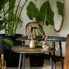 Decorative Ananas Votive with other  objects on table like bronze monkey and rabbit figurines, surrounded by plants.