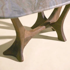 Close-up of a table with sculptural wooden legs and a marble top, photographed on a warm cream surface.