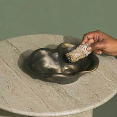 Hand holding sage bundle over a stone bowl on a stone surface with a green background