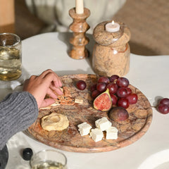 Person reaching for a cracker on a wooden board with cheese, figs, and grapes.