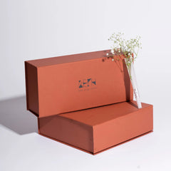 Red gift box with branding with a floral arrangement on a light gray background
