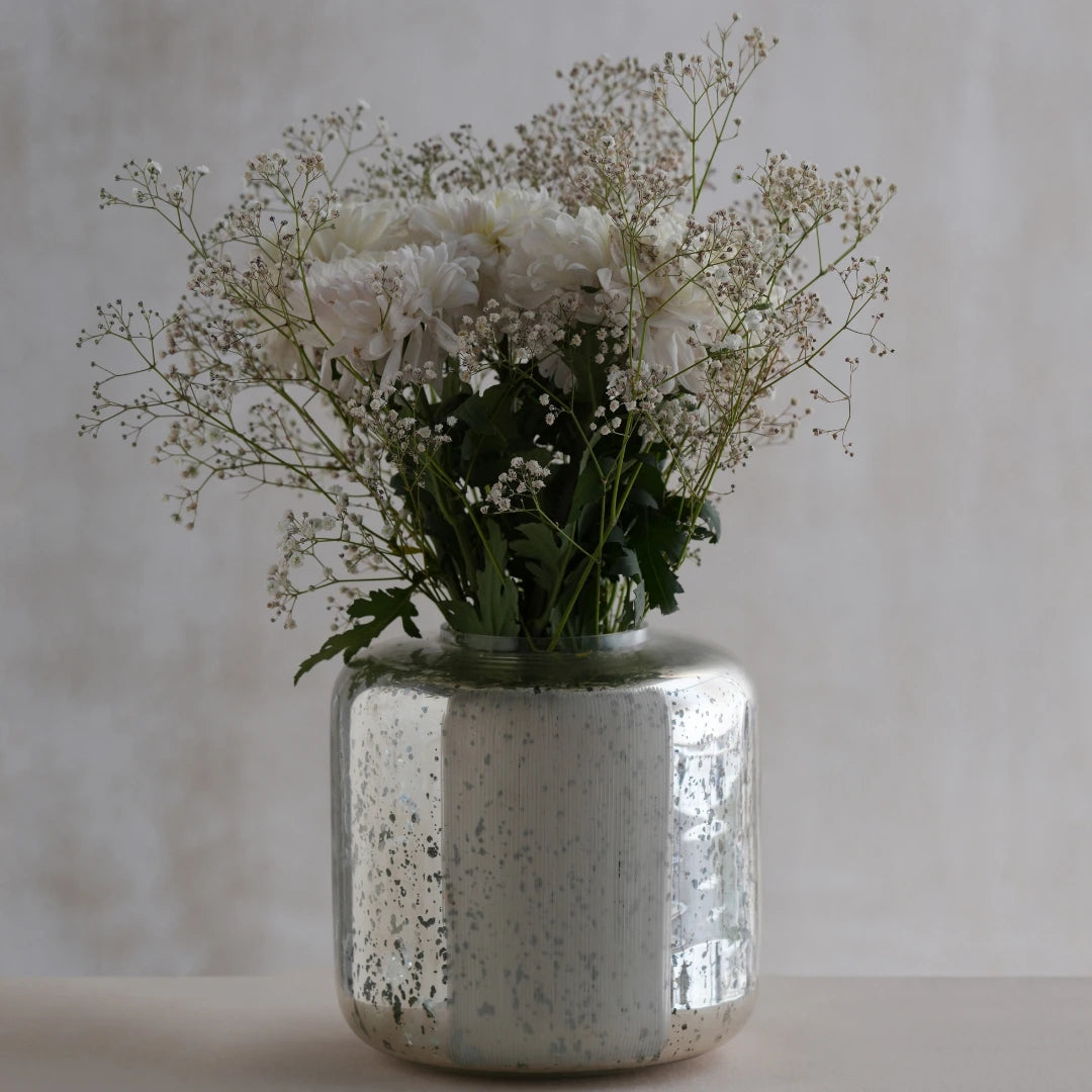 Decorative silfr vase made of glass with white flowers and greenery on a neutral background