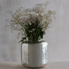 Decorative silfr vase made of glass with white flowers and greenery on a neutral background