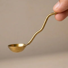 Muun Ghee Daani curved serving spoon with wavy handle held in hand, brass-antique finish, close-up