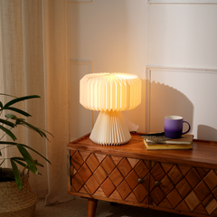 A white origami paper table lamp with a pleated design, warm lighting placed on a wooden console