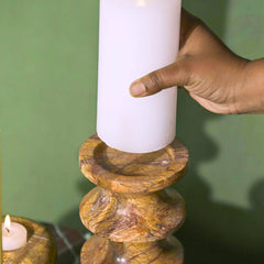 Hand placing a white candle into a Astra Brown Marble Candle Holder against a green background