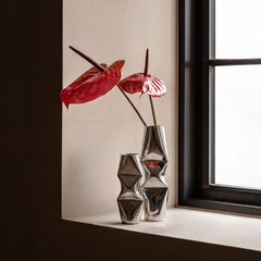 Chrome Dented Vases with sculptural, faceted geometric designs, arranged on a windowsill next to a window with red anthurium flowers.