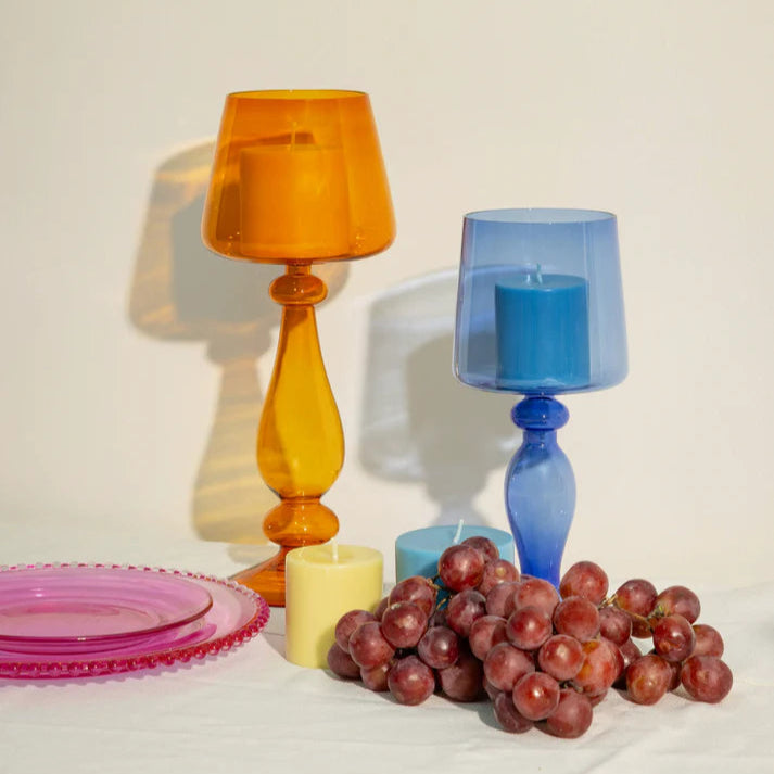 Two colorful glass candle holders with grapes and plates on a light surface.