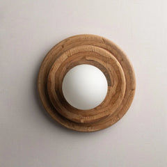Tiered wall-mounted light fixture with a natural wood concentric frame and a white frosted glass globe shade, shown against a plain light gray wall.