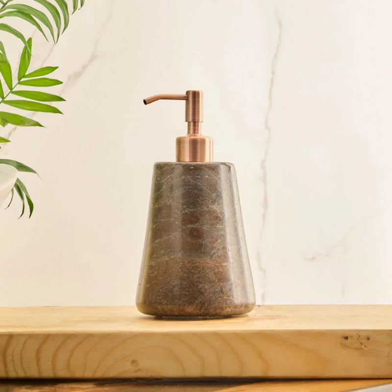 Reen Dark Soap Dispenser with a textured brown stone body and a metallic copper pump, resting on a light wood surface against a white background.