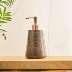 Reen Dark Soap Dispenser with a textured brown stone body and a metallic copper pump, resting on a light wood surface against a white background.