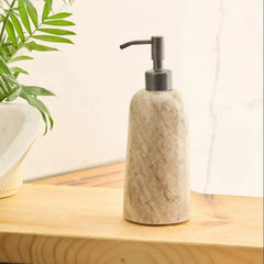 A marble-textured Rower soap dispenser with a dark metal pump, sitting on a light wood surface next to a potted plant. 