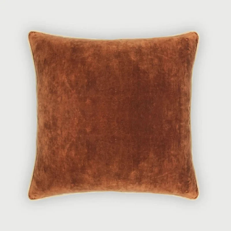 A square throw pillow in a warm rust-brown velvet fabric, shown against a light gray background.