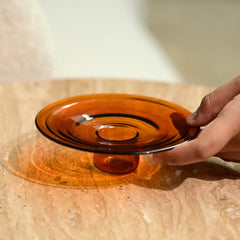Hand holding a transparent amber glass incense Holder on a wooden surface