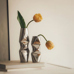 Two modern metallic silver Chrome Dented Vases with tulips, styled on a white surface against a warm beige background.